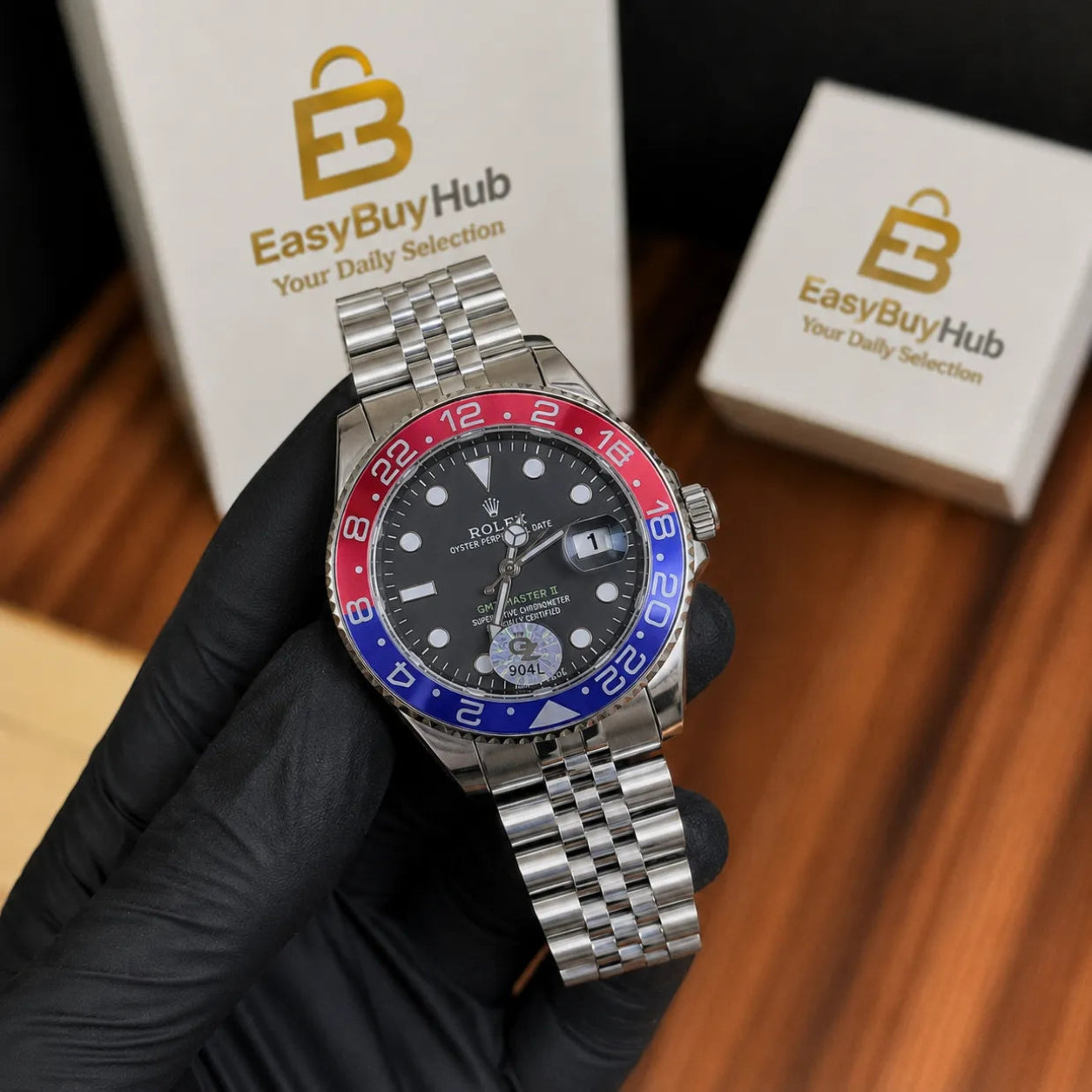 A Rolex Submariner Date watch with a black dial and a red and blue bezel, held by a hand wearing a black glove. Two white boxes with the EasyBuyHub logo are visible in the background on a wooden surface.