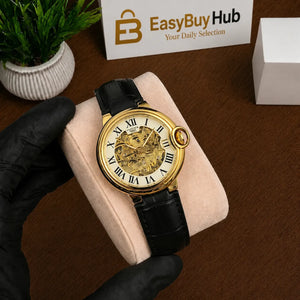 A luxury watch with a gold-tone case, skeleton dial, and black leather strap, held by a black-gloved hand on a beige cushion. The background shows a wooden table, a small potted plant, and a 'EasyBuy Hub' sign.