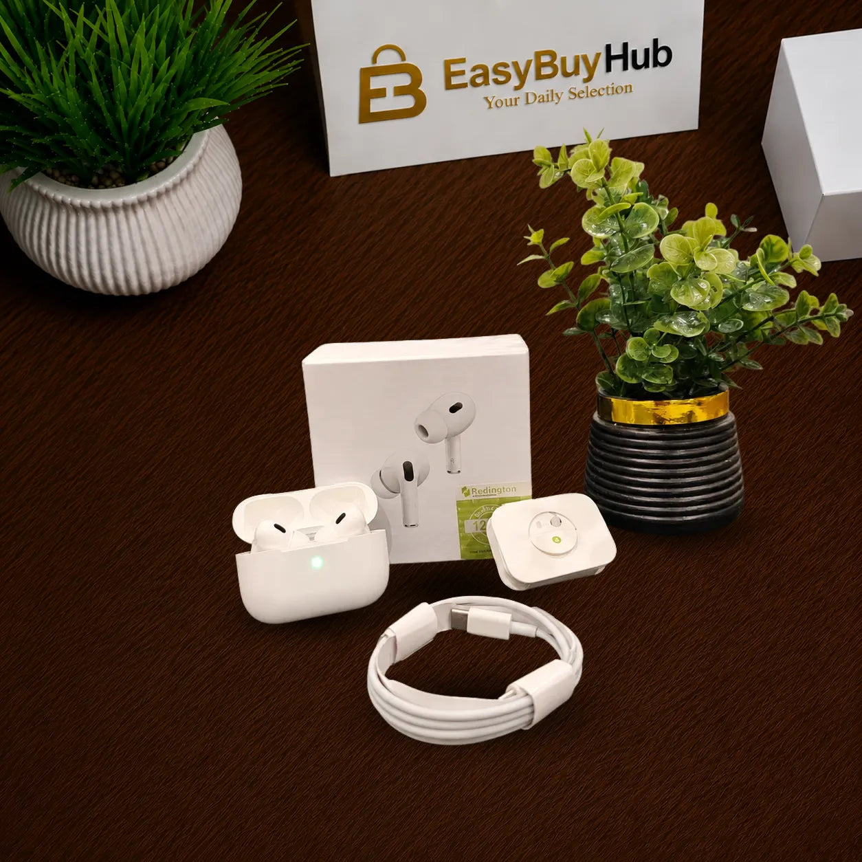 A white wireless earbud charging case, a coiled white charging cable, a small round white device, and the product box are arranged on a dark brown textured surface. Two potted green plants and a branded EasyBuyHub sign are visible in the background.