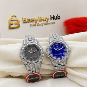 Two luxury-style wristwatches with diamond-encrusted silver-tone cases and link bands, displayed on draped cream fabric. One watch has a dark gray dial, and the other has a vivid blue dial.