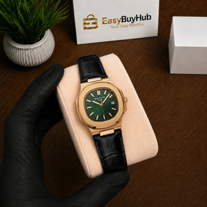 A gold-tone wristwatch with a dark green dial and black leather strap, resting on a beige display cushion held by a black-gloved hand. A branded EasyBuyHub box and a small potted plant are visible in the background on a wooden surface.