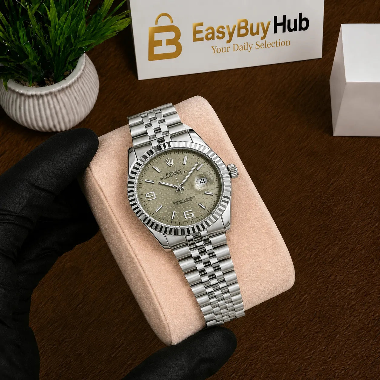 A Rolex Oyster bracelet watch with a silver stainless steel case and a champagne-gold dial, displayed on a beige cushion held by a hand in a black glove. A 'EasyBuyHub' store sign is visible in the background on a wooden table.