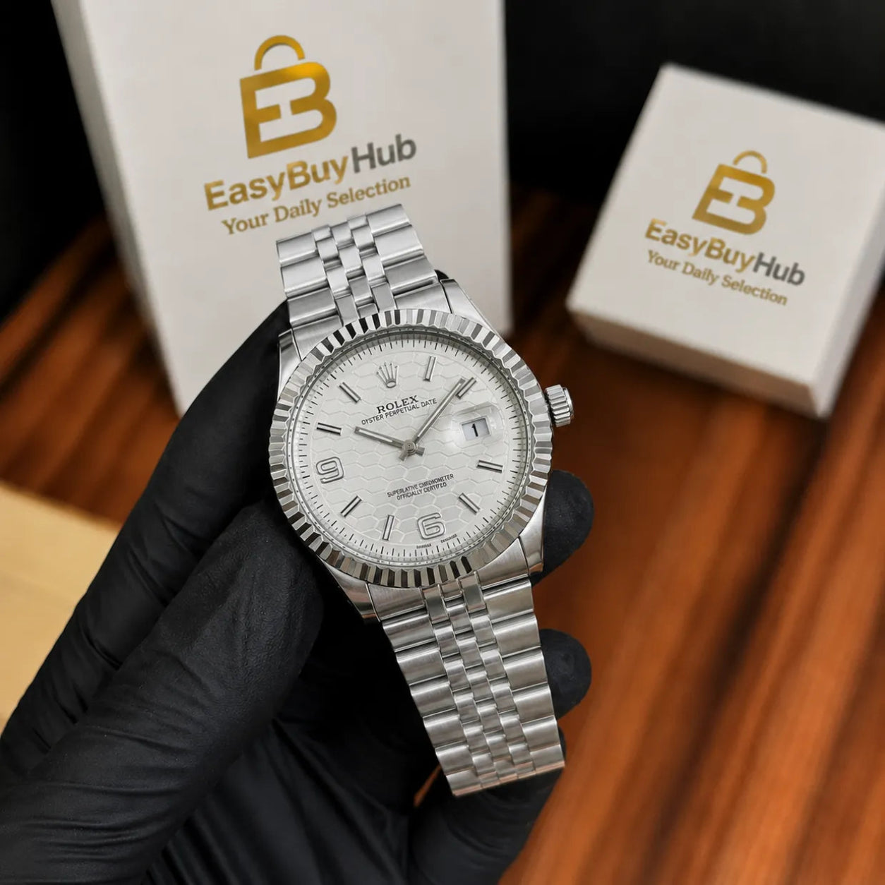 A silver Rolex Datejust watch with a white dial and fluted bezel, held by a hand wearing a black glove. Two white EasyBuyHub boxes are visible in the background on a wooden surface.