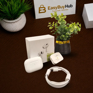 A wireless earbud charging case set with its white retail box, a white charging cable, a small white square accessory, and a small round tracker-like device, arranged on a dark brown tabletop with decorative plants and a branded EasyBuyHub sign in the background.