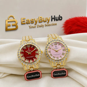 Two gold-tone wristwatches with crystal-encrusted bezels are displayed on a white draped fabric. The left watch has a red dial and the right watch has a pink dial, both with gold-tone hands and markers.
