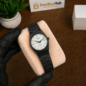 A wristwatch with a black metal case and link bracelet, featuring a white dial, displayed on a beige cushion held by a hand wearing a black glove. The background shows a wooden table, a small potted plant, and a box labeled 'EasyBuyHub'.